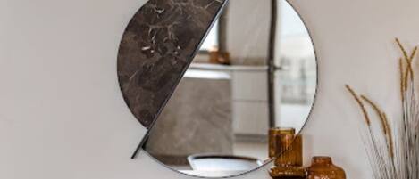 A round mirror with a marble-like surface, mounted on a wall above a wooden dresser with a white countertop.