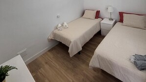 Una habitación pequeña y limpia con dos camas individuales, una mesita de noche con lámpara y una planta en maceta.