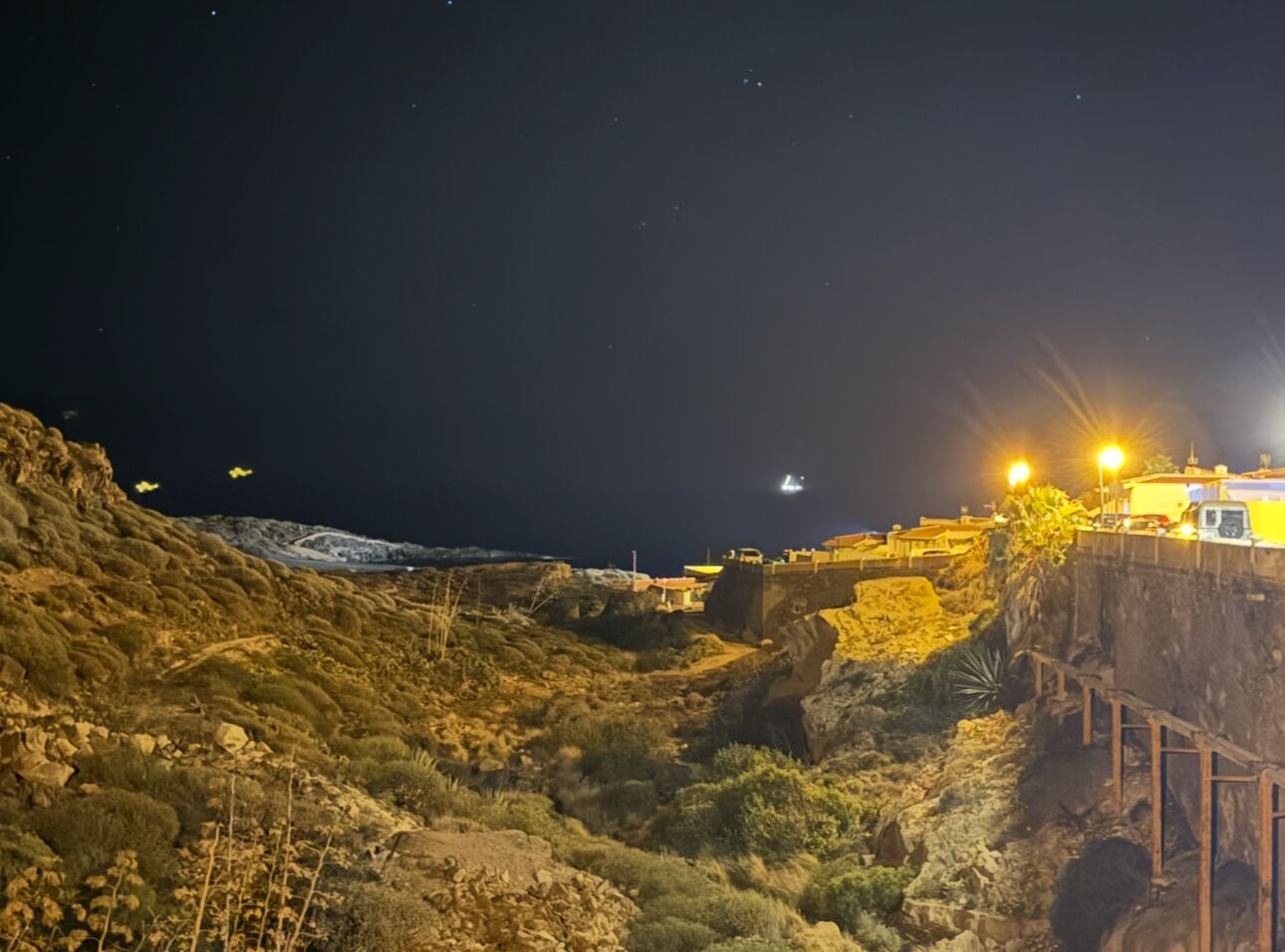 Un paisaje costero nocturno con terreno rocoso y una estructura con luces brillantes.