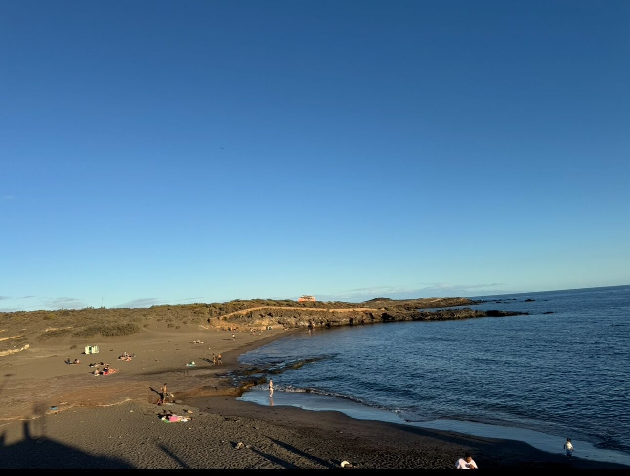 A beach with a rocky shoreline, a few people, and a clear sky.