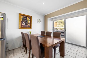 A dining area with a wooden table, six chairs, a clock, and a framed picture on the wall.