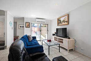 Ein modernes Wohnzimmer mit einem blauen Sofa, einem Glastisch und einem Flachbildfernseher auf einem Holzboden.