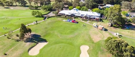 An aerial view of a golf course with a clubhouse, sand bunkers, and surrounding trees.
