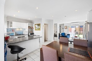 Eine moderne Küche mit weißen Schränken, ein Essbereich mit einem Holztisch und Stühlen sowie ein Wohnzimmer mit einem blauen Sofa und einem Couchtisch.