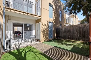 A residential property with a patio, a sliding glass door entrance, a small outdoor seating area, and a wooden fence.