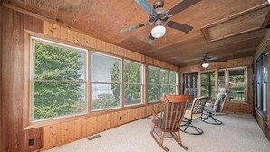 A room with large windows, wooden walls, a ceiling fan, and two rocking chairs.