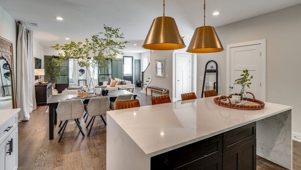 Een moderne keuken met een groot eiland, hanglampen en een eethoek met uitzicht op de woonkamer.