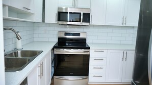 A modern kitchen with white cabinets, stainless steel appliances including a microwave, oven, and refrigerator, and a double sink.