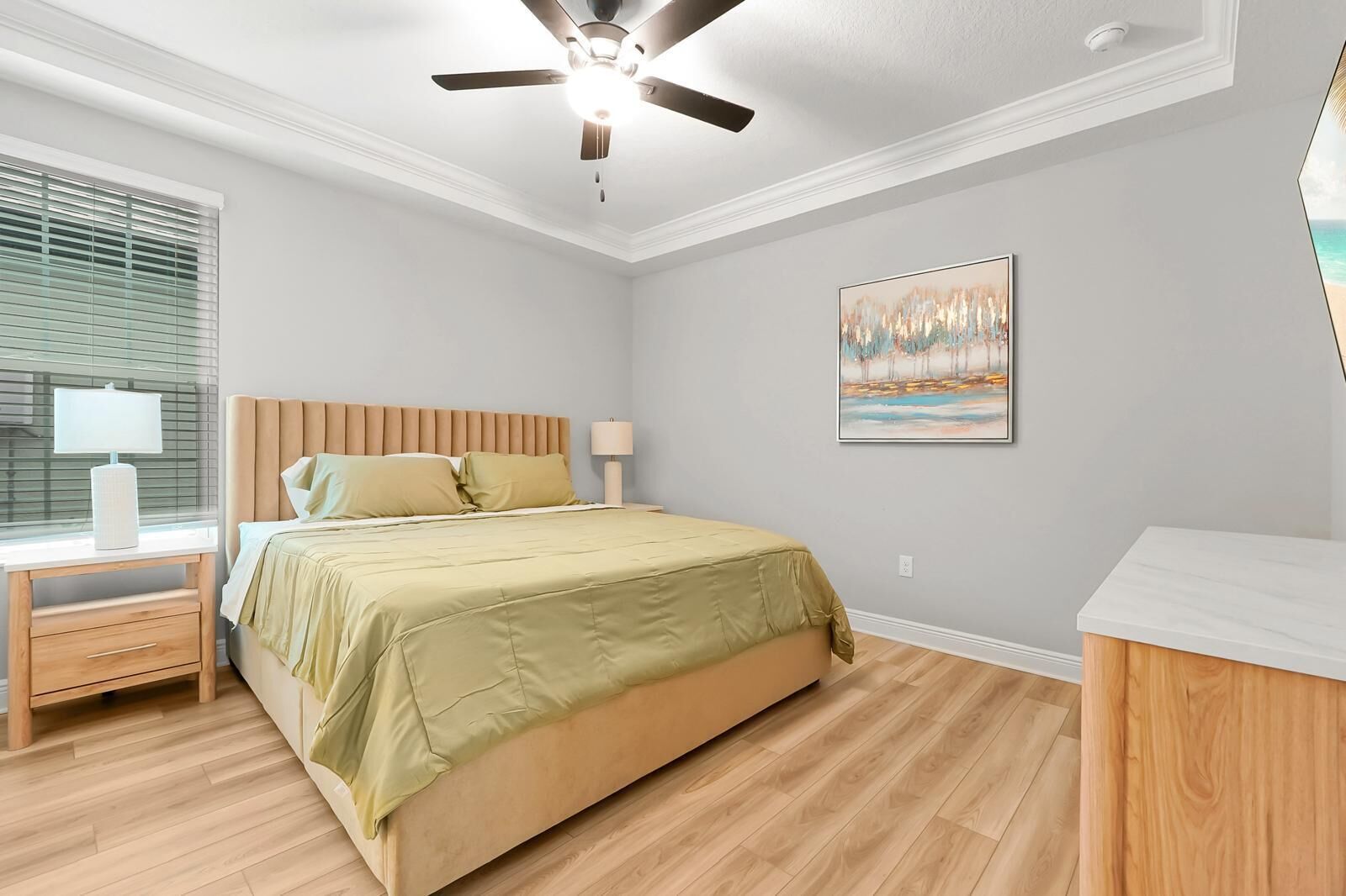 Un dormitorio con cama, mesita de noche, lámpara, ventilador de techo y un cuadro en la pared.