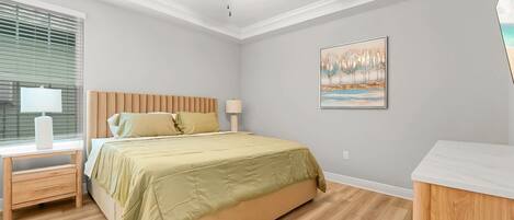 Un dormitorio con cama, mesita de noche, lámpara, ventilador de techo y un cuadro en la pared.