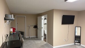 Una habitación con una mesa de comedor, sillas, un televisor montado en la pared y una puerta que da a un baño.
