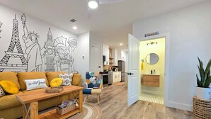 A modern living room with a wooden coffee table, a sofa with yellow cushions, and a wall mural featuring famous landmarks. - The Global Citizen (Pensacola)