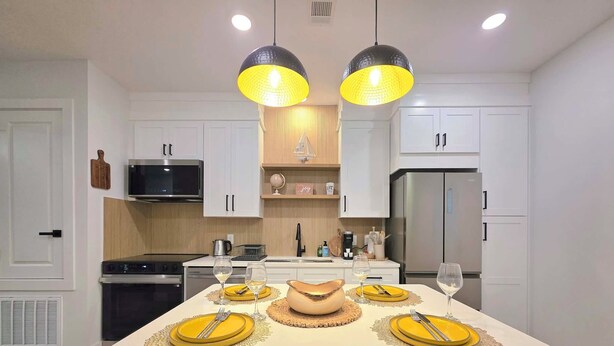A modern kitchen with white cabinets, a central island with yellow placemats, and two pendant lights. - The Global Citizen (Pensacola)
