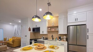 A modern kitchen with white cabinets, a stainless steel refrigerator, and a dining area with yellow chairs and a central island. - The Global Citizen (Pensacola)