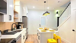 A modern kitchen with white cabinets, a central island with yellow stools, and a staircase with white railings. - The Global Citizen (Pensacola)