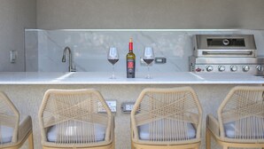 An outdoor bar area with a wine bottle, two glasses, a grill, and wicker chairs. - 10BR Golden Pear Villa-MS, Sea View – Family/Group Ready (Saint George)