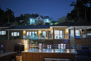 A modern hotel with a pool area, large windows, and solar panels. - 10BR Golden Pear Villa-MS, Sea View – Family/Group Ready (Saint George)