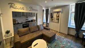 A living room with a brown sofa, a small round table, a kitchen in the background, and a wall with 'Relax & Dream' text. - This one bedroom is located in a beautiful Historic Villa in Landstuhl, Germany (Landstuhl)