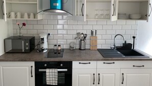 A modern kitchen with white cabinets, a blue range hood, a coffee maker, and a built-in oven. - This one bedroom is located in a beautiful Historic Villa in Landstuhl, Germany (Landstuhl)