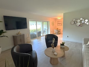 Ein Wohnzimmer mit Flachbildfernseher, zwei Ledersesseln, einem Couchtisch und einem Essbereich mit Tisch und Stühlen.