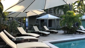 Ett område vid poolen med solstolar och parasoller, en pool med en skylt som förbjuder dykning och en varningsskylt för badvakten.