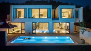 Ein modernes, zweistöckiges Haus mit großen Fenstern, einem Swimmingpool und einem hellen Innenraum.