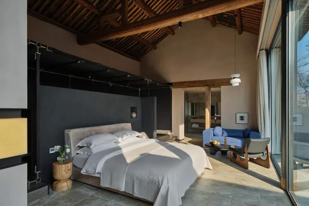 A modern bedroom with a large bed, a wooden ceiling, and a view of the outside.