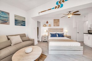 Un dormitorio moderno con una cama, un sofá, una mesita y un ventilador de techo.