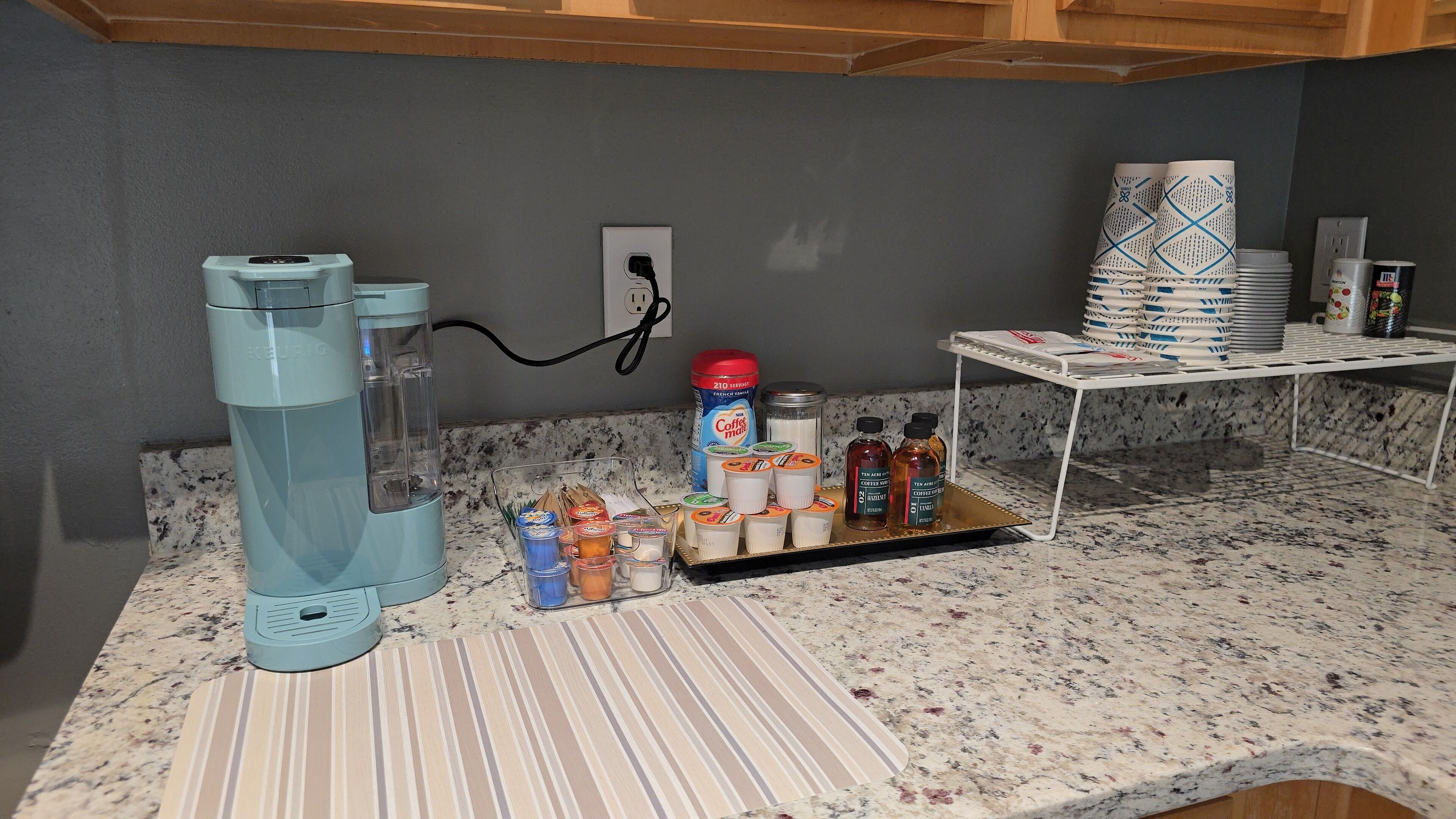 Un comptoir de cuisine avec une cafetière, une machine à café, un pot à lait et un plateau contenant divers condiments.