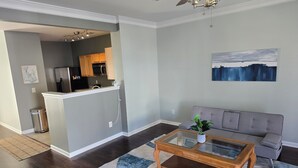 Ein modernes Wohnzimmer mit einem Glastisch, einem grauen Sofa und einer Küchenzeile mit Holzausbau und einem Edelstahlkühlschrank.