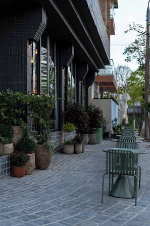 Un bâtiment à la façade sombre, agrémenté de plantes en pot et doté d’un espace extérieur aménagé pour s’asseoir.
