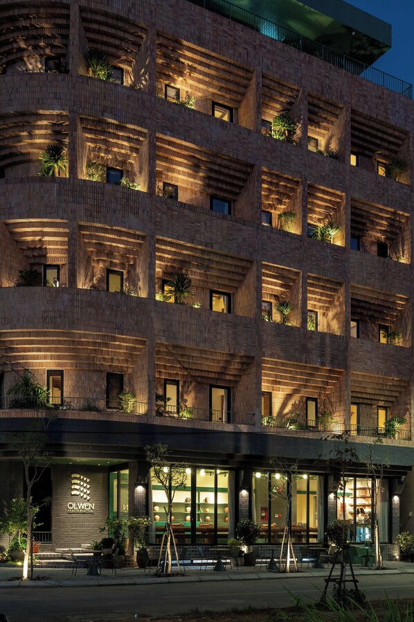 A multi-story hotel with a brick facade, balconies with plants, and a well-lit entrance. - Olwen Boutique Hotel (Da Nang)