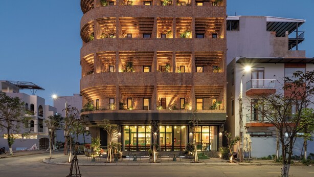 A multi-story building with a curved facade, balconies with plants, and a ground-level entrance with seating. - Olwen Boutique Hotel (Da Nang)