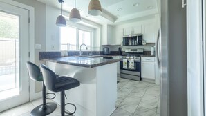 Una cocina moderna con una isla central, taburetes de bar, iluminación colgante y electrodomésticos de acero inoxidable.