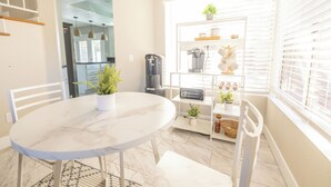 Una cocina moderna con una mesa de mármol, sillas blancas, una cafetera, un tostador y una ventana con persianas.
