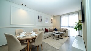 Ein modernes Wohnzimmer mit Essbereich, einer Sofagarnitur und einem an der Wand befestigten Fernseher.