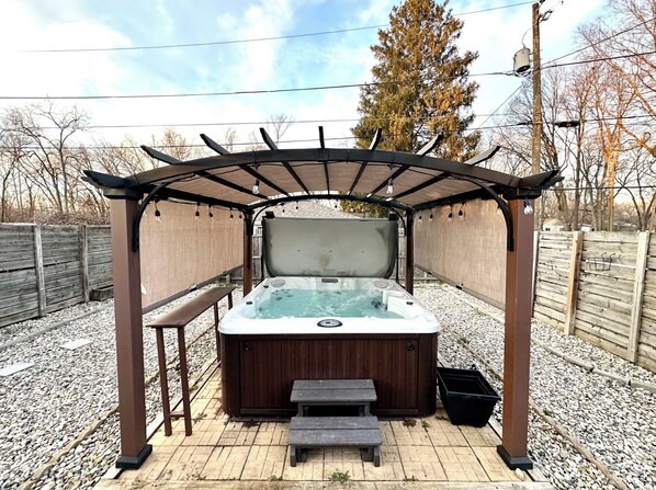Un bain à remous installé sous une pergola, avec une terrasse en bois et des marches menant à celle-ci.