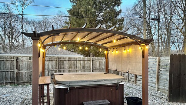 A hot tub under a wooden pergola with string lights, surrounded by a wooden fence and gravel. - Hot tub getaway quiet 2bdrm home in N. Broad Ripple (Indianapolis)