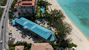 An aerial view of a hotel with a blue-roofed building, a pool, and a beach.