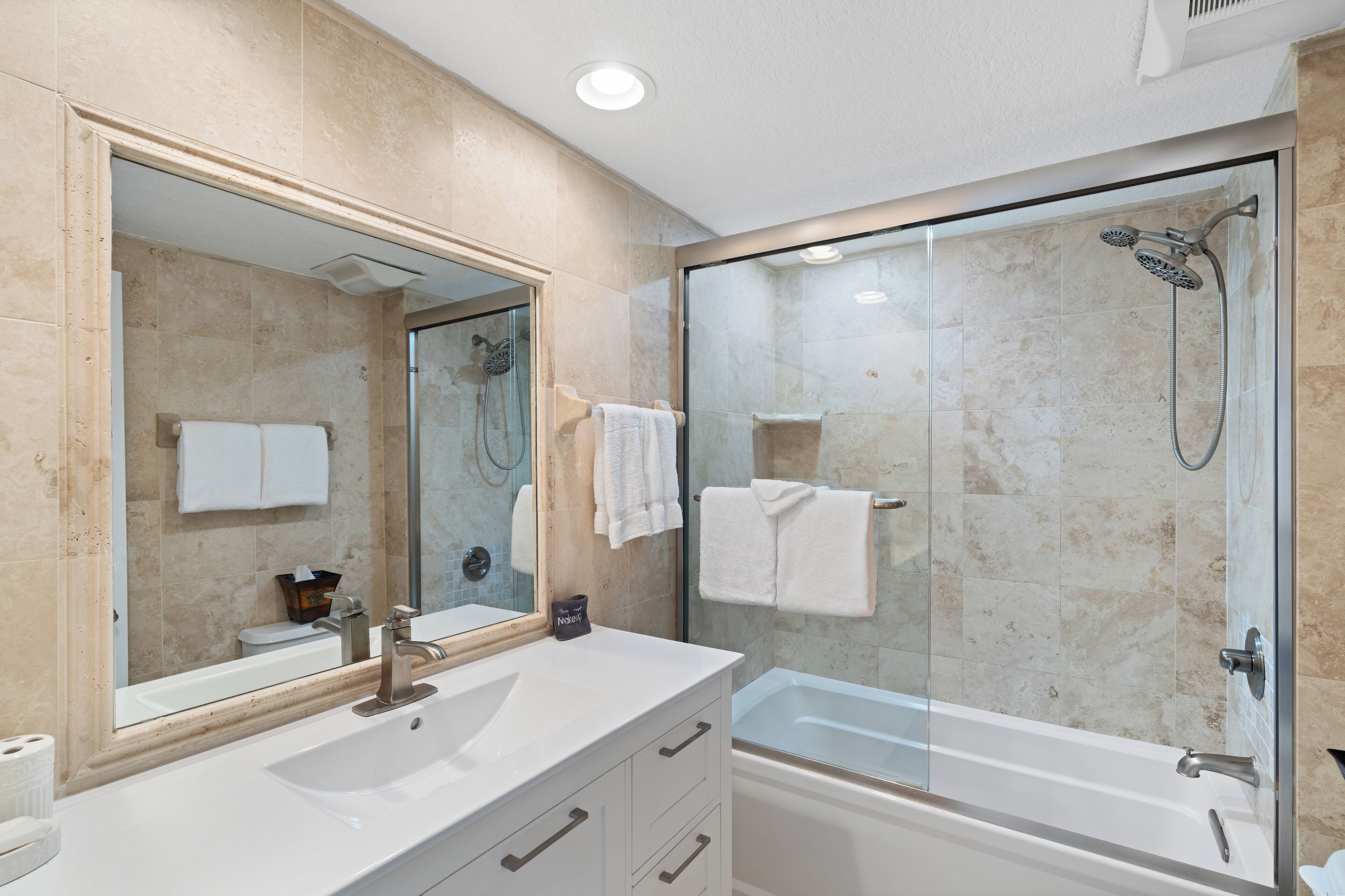 A modern bathroom with a glass-enclosed shower, a large mirror, and a white sink.