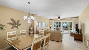 A dining area with a wooden table and chairs, a chandelier, and a view of the outdoors through large windows.