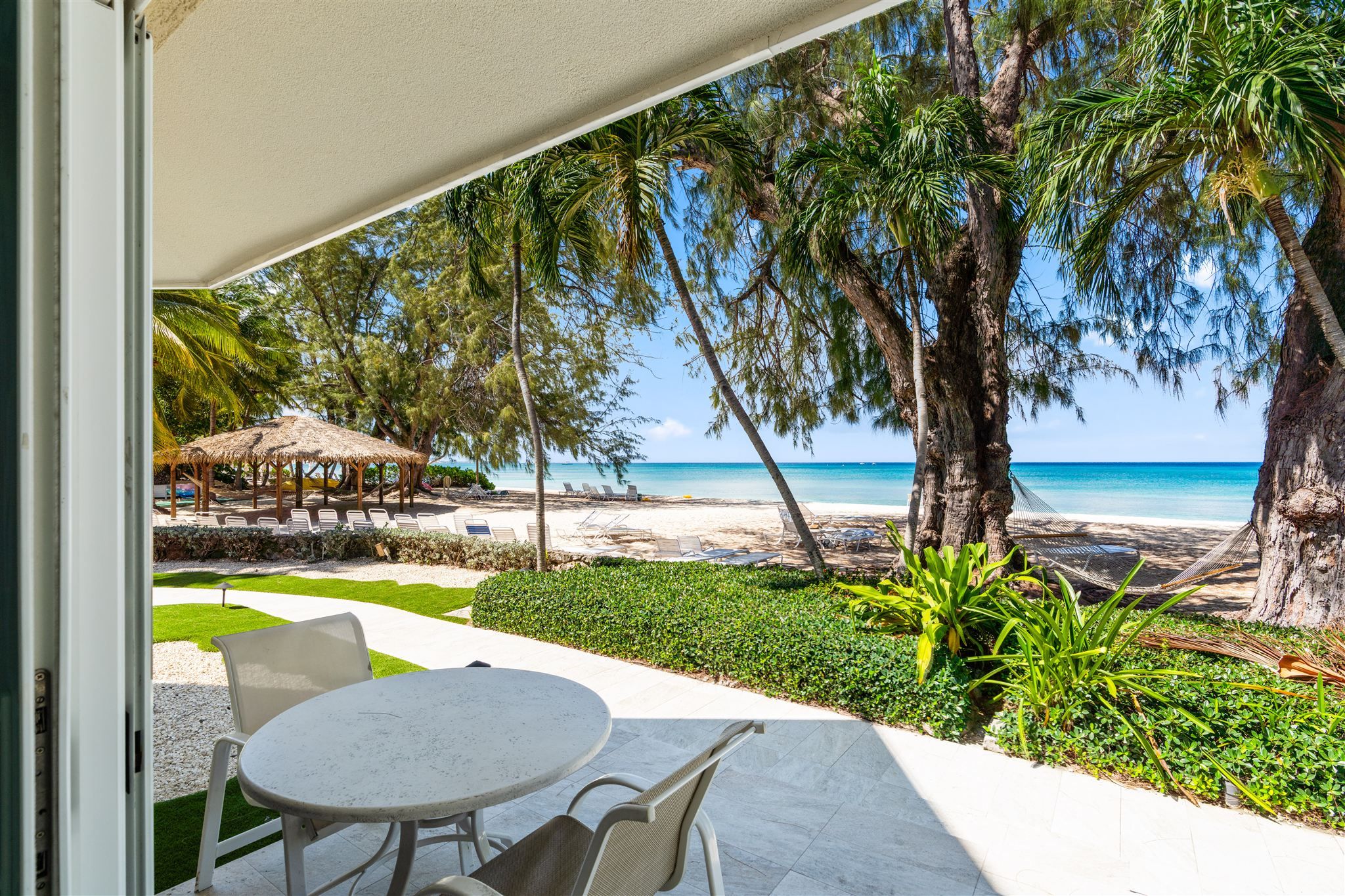 Une terrasse avec une table et des chaises, donnant sur une plage bordée de palmiers et surplombant un ciel bleu azur.