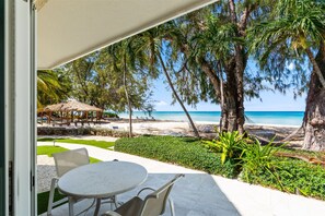 Une terrasse avec une table et des chaises, donnant sur une plage bordée de palmiers et surplombant un ciel bleu azur.
