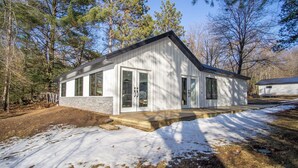 Un bâtiment moderne de plain-pied, doté de grandes fenêtres et d’une fondation en pierre, entouré d’arbres et de neige.