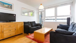 A modern living room with a flat-screen TV, two sofas, a wooden cabinet, and large windows. - Bright & Spacious 2 Bed Islington Flat | Fast Wi-Fi (London)
