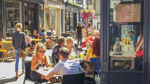 An outdoor café with tables and chairs, people dining, and a storefront with a sign. - Bright & Spacious 2 Bed Islington Flat | Fast Wi-Fi (London)