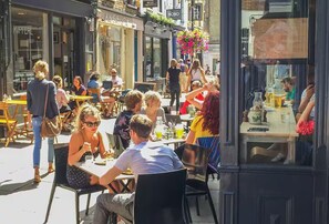 An outdoor café with tables and chairs, people dining, and a storefront with a sign. - Bright & Spacious 2 Bed Islington Flat | Fast Wi-Fi (London)