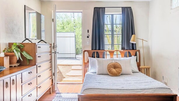 A bedroom with a wooden bed, a dresser, a mirror, and a window with curtains. - Bungalow + Casita With Private Patios Near Downtown / U of A (Tucson)