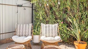 Two wicker chairs with patterned cushions, a potted plant, and a striped wall in a patio setting. - Bungalow + Casita With Private Patios Near Downtown / U of A (Tucson)