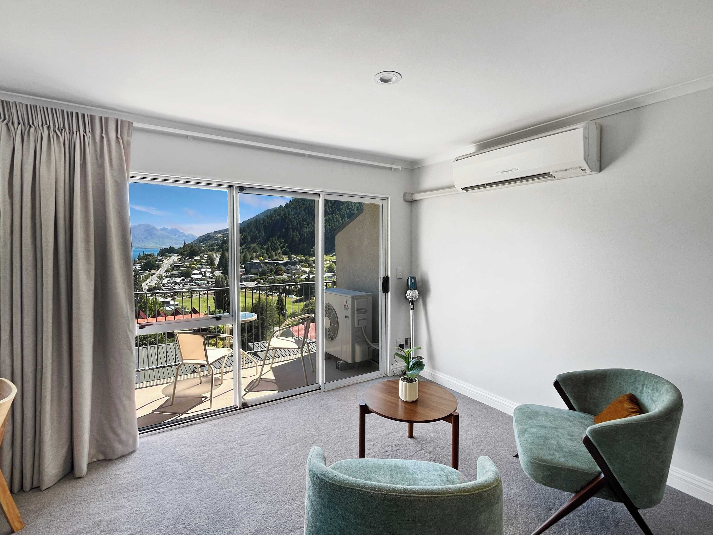 Une pièce avec vue sur la ville et les montagnes, une porte-fenêtre coulissante, une petite table avec une plante et deux chaises.
